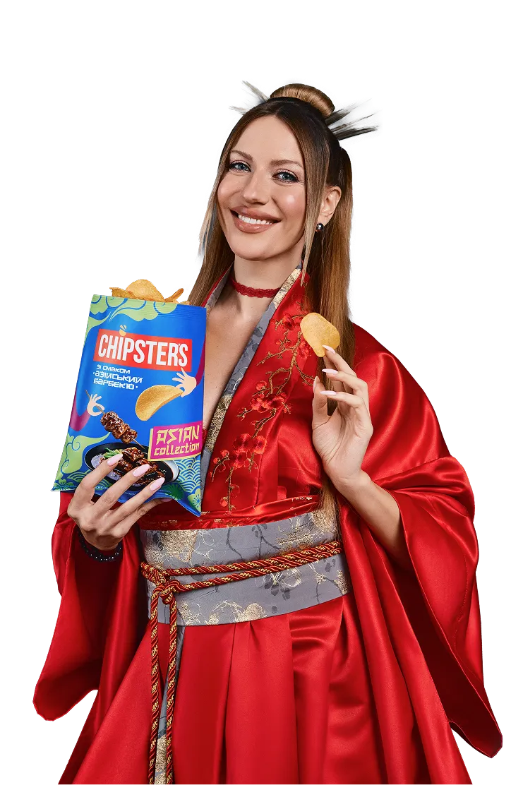 Леся тримає пачку Chipsters зі смаком азійський барбекю посміхаючись показує чипсу в лівій руці