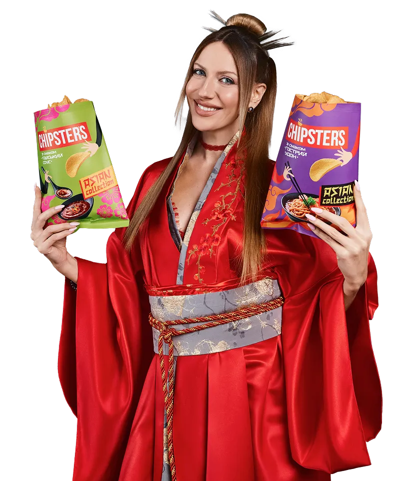 Леся посміхаючись тримає дві пачки Chipsters зі смаком азійський барбекю та гострий удон